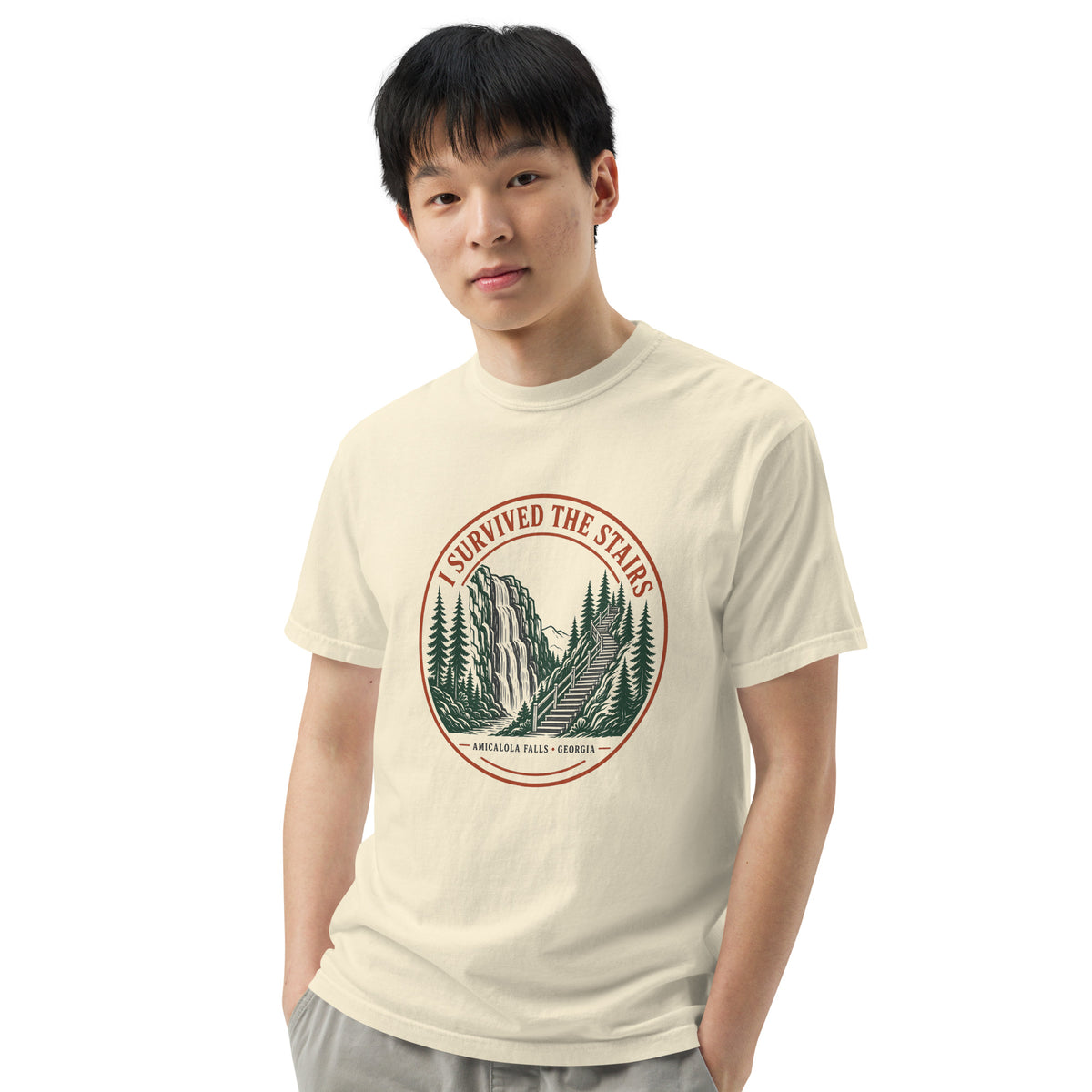 Model in the ivory I Survived the Stairs tee, angled pose with hands in pockets, showing the Amicalola Falls, Georgia waterfall and staircase badge