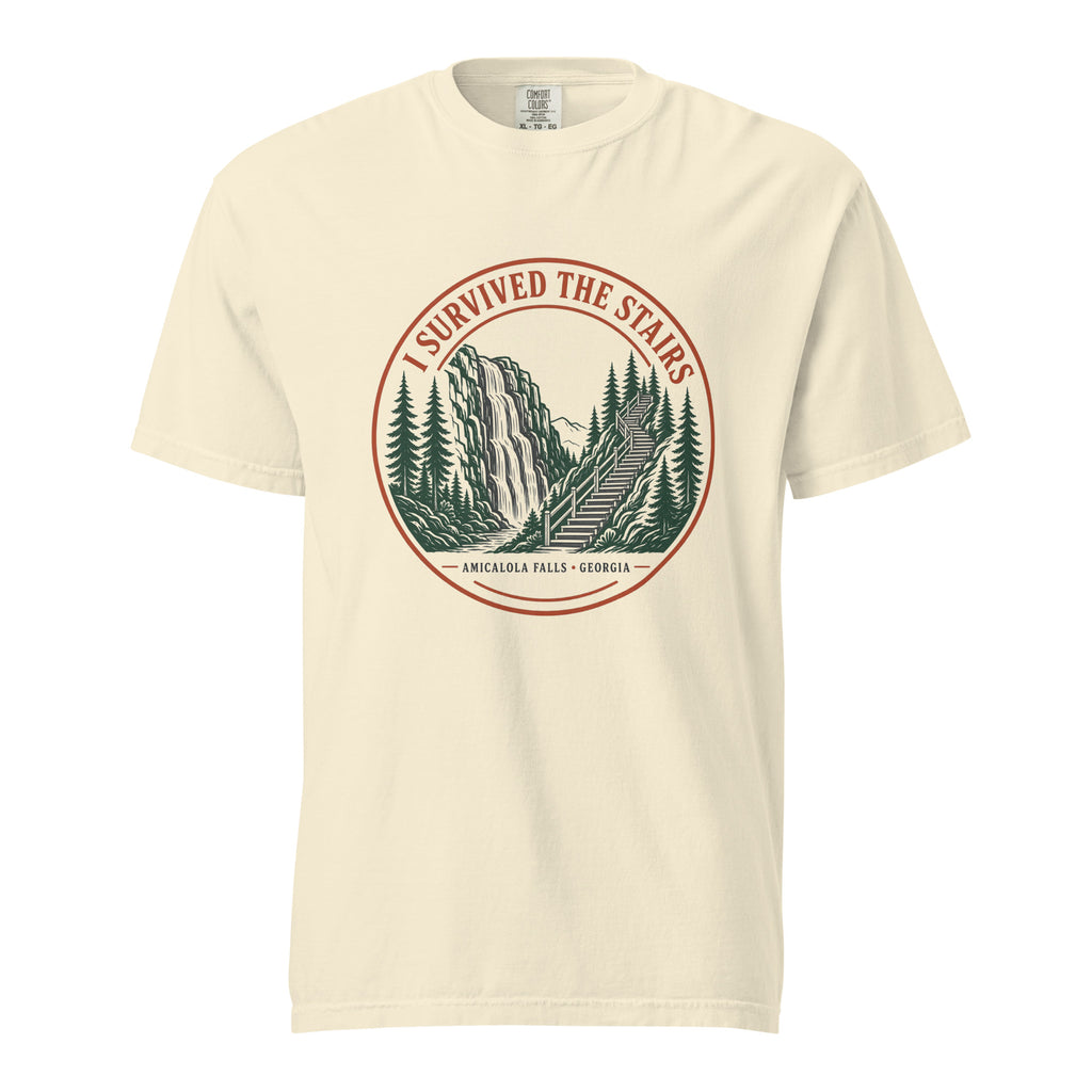 Ivory Comfort Colors tee, flat front view, with a round red and green 'I Survived the Stairs' badge showing Amicalola Falls and the trail staircase through pine trees