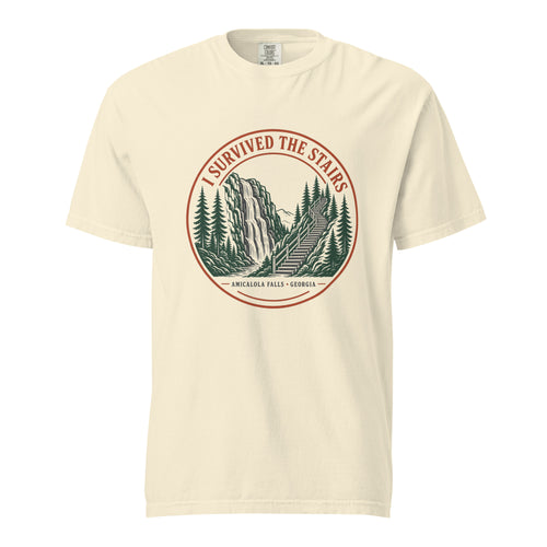 Ivory Comfort Colors tee, flat front view, with a round red and green 'I Survived the Stairs' badge showing Amicalola Falls and the trail staircase through pine trees
